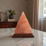 Handcrafted pyramid shape table lamp with smooth angled facets carved from Himalayan pink salt mounted on a stepped wooden base