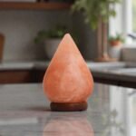 Handcrafted illuminated tear drop table lamp carved from Himalayan pink salt mounted on a circular dark wooden base