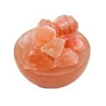 Handcrafted pink salt bowl with natural shape salt chunks and dark polished wooden base filled with rough rock salt crystals