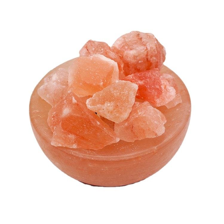 Handcrafted pink salt bowl with natural shape salt chunks and dark polished wooden base filled with rough rock salt crystals