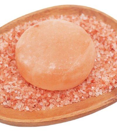 Handcrafted smooth round Himalayan pink salt massage stone resting on coarse pink rock salt crystals within a wooden dish