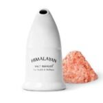 White ceramic Himalayan salt inhaler with mouthpiece standing next to a pile of coarse pink rock salt crystals